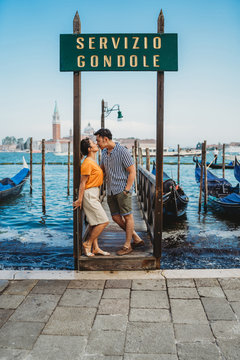 Loving couple on vacation in Venice - Millennials kiss on the boat platform - Sign with "Gondola Service" written in Italian