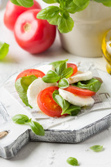 Caprese salad with mozzarella, juicy tomato and fresh Basil. Delicious Italian snack, traditional food. On light background