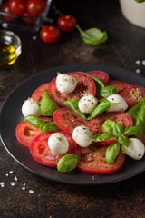 Caprese salad with mini mozzarella, juicy tomato and fresh Basil. Delicious Italian snack, traditional food. On dark background