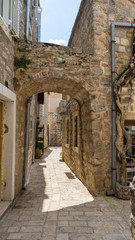 Fototapeta na wymiar Picturesque narrow street in old town of Budva, Montenegro. Ancient houses. Stone arch inside the fortress