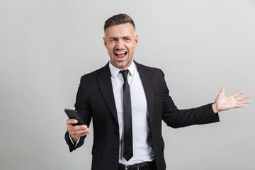 Image of excited handsome businessman in formal suit typing on cellphone and celebrating victory