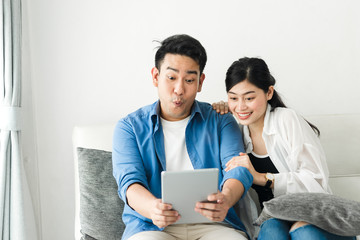 Surprising Asian couple using tablet at home, lifestyle concept.