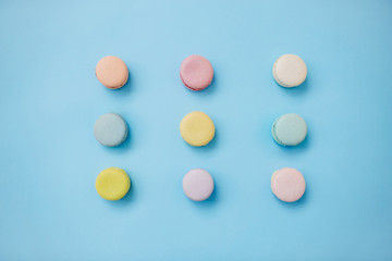 Top view of sweet colorful French macaroon biscuits lying in three lines on pastel blue backgroud.
