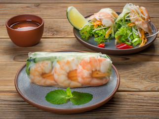 Close Up view of Vietnamese spring rolls with shrimps on two plates on wooden background. Soft focus.