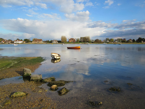 A tranquil scene with boats in a seaside harbour with blue sky and white clouds reflecting in calm mirror like water. Bosham. UK - Image