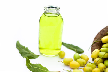 Fresh green neem fruit of Indian Lilac fruit in a clay bowl isolated on white along with its oil in a transparent glass bottle.Horizontal shot.
