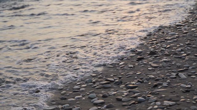 Waves beat on pebbles on the sandy shore of the Black Sea in the evening.