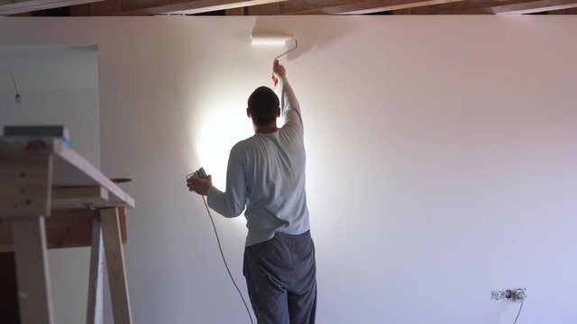 repair of the apartment - professional painter paints the walls with white paint roller