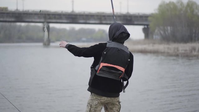 Young fisherman in the early morning catch scomber fish with spinning in river near the city. Fun or joke. Raffle or incredible.