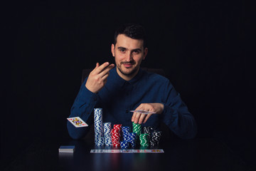 Confident guy poker player seated at the casino table throwing playing cards over black background....