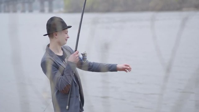 Young fisherman in a jacket and a cap with a brim in the early morning catch scomber fish with spinning in river near the city