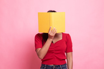 Young Asian woman with a book cover her face.