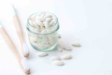 toothpaste tablets in a glass jar with bamboo toothbrushes on white background, eco friendly zero waste living concept.