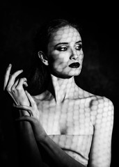 Beautiful girl model with red lips make up and naked shoulders covered with a shadow mask in the form of a net of hexagonal honeycomb. Close up. Black and white. Conceptual fashion design.