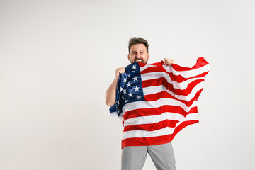 Celebrating an Independence day. Stars and Stripes. Young man with the flag of the United States of America isolated on white studio background. Looks crazy happy and proud as a patriot of his country