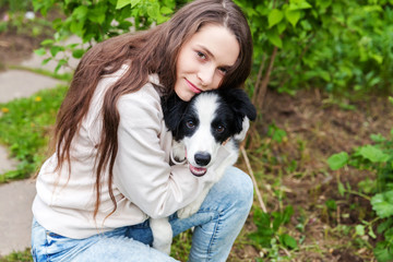 Smiling young attractive woman embracing cute puppy dog border collie in summer city park outdoor background. Girl huging new lovely member of family. Pet care and animals concept