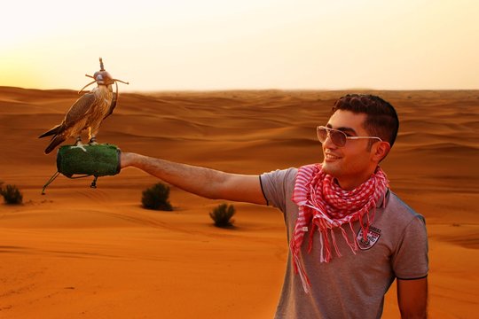portrait of a young man with a falcon on his hand in a desert at sunset