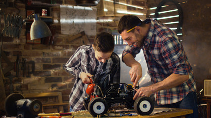 Father and son are working on a radio control toy car in a garage at home.