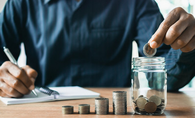 Men are Saint documents about save money and put coin in glass jar on desk.