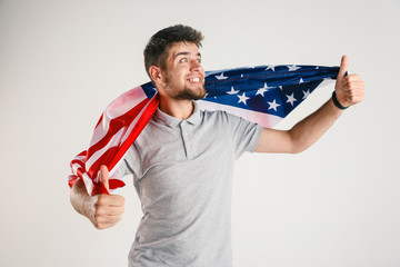 Celebrating an Independence day. Stars and Stripes. Young man with the flag of the United States of America isolated on white studio background. Looks crazy happy and proud as a patriot of his country