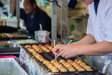 Moving hand of street food chef making takoyaki traditional Japanese food.