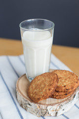 still life of round brown wholegrain flour cookies and milk glass on striped white napkin on wooden table, angle above view of vertical stock photo image