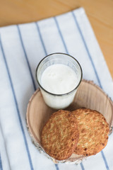 still life of round brown wholegrain flour cookies and milk glass on striped white napkin on wooden table, top view of vertical stock photo image with copy space for text