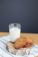still life of round brown wholegrain flour cookies and milk glass on striped white napkin on wooden table, side view of vertical stock photo image with copy space for text