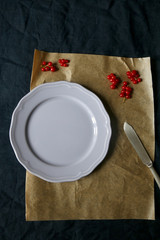 Table setting with navy tablecloth, parchment paper, one lilac plate, antique knife and red currants. Top view, copy space.