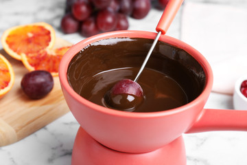 Dipping grape into pot with chocolate fondue on table, closeup