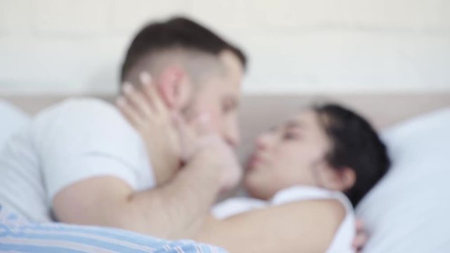 selective focus of happy man kissing nose and hand of attractive woman while lying on bed 