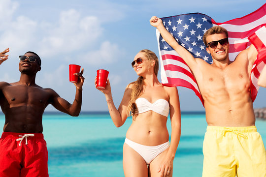 summer, holidays and people concept - group of happy friends with flag and non alcoholic drinks celebrating american independence day and party over beach background in french polynesia - Powered by Adobe