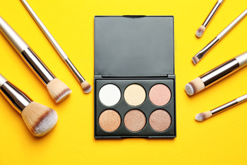 Flat lay composition with professional makeup brushes and eye shadow palette on yellow background