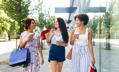 sale, friendship and people concept - happy young women with shopping bags and takeaway drinks walking along city street