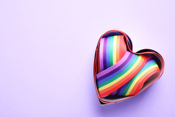 Heart shaped mold and bright rainbow ribbon on color background, top view with space for text. Symbol of gay community