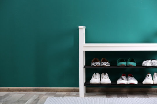 Shoe rack with different footwear near color wall, space for text. Stylish hallway interior