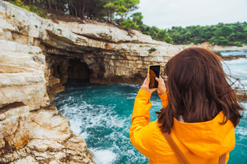 young woman sitting at cliff looking at grotto cave with blue azure water. taking picture
