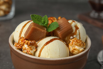 Delicious ice cream with caramel and popcorn in bowl on table, closeup