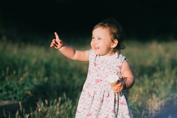 Little, charming girl in a dress in the summer eating ice cream at sunset