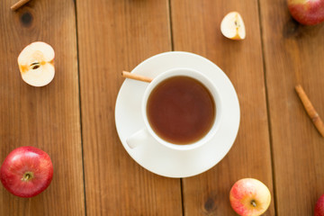 Obraz na płótnie Canvas objects and drinks concept - cup of black tea with apples and cinnamon on wooden table