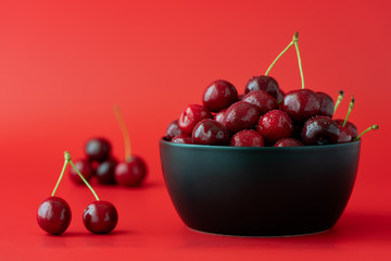 Freshly picked cherries in a black ceramic bowl. Bright red background, water drops, negative space, high resolution