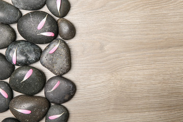 Spa stones with flower petals on wooden background, flat lay. Space for text