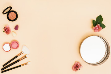 Blender; makeup brushes; rose; mirror and compact powder on beige background