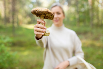season, nature and leisure concept - young woman holding mushroom in autumn forest