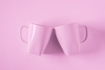 Pink coffee mugs on pink background clinking in cheers with empty copyspace