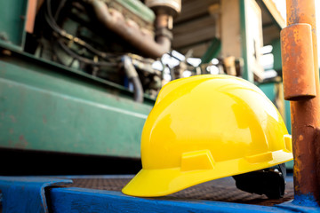 Yellow hardhat or safety helmet is placed on working platform of pumping unit in oil field operation. Selected focus on the hard hat. Safety, no accident in workplace concept