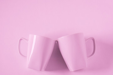Pink coffee mugs on pink background clinking in cheers with empty copyspace