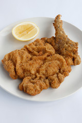 Succulent Traditional Italian Crummed and  Deep Fried Veal Cutlet or (Cotaletta alla Milanese) presented on an isolated white plate and white background with a slice of lemon
