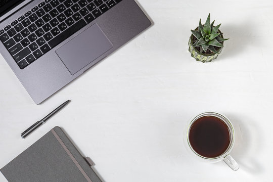 Workplace freelancer. Grey modern laptop with russian keyboard, cup of coffee, metallic pen, green succulent, copybook on light background with copy space. Top view. Flat lay.