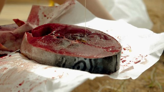Close-up shot of female hand rubbing olive oil to a fillet of tuna fish. Slow motion. HD